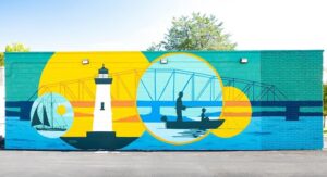 A mural painted on building. It depicts a water scene with a bridge, fisherman, lighthouse, and sailboat.
