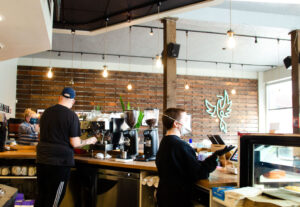 Employees behind the counter of a coffee shop, wearing masks.