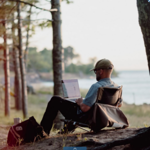 A person works on a laptop in front of a lake.