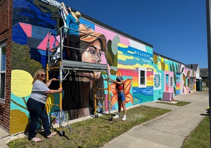People working on a colorful mural on the side of local business.