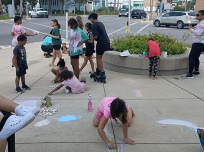 Several children playing and drawing on the sidewalk with chalk.