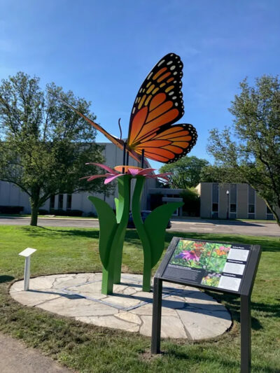 Large, metal Monarch Butterfly sculpture in a park. In front of the sculpture is an informational placard.