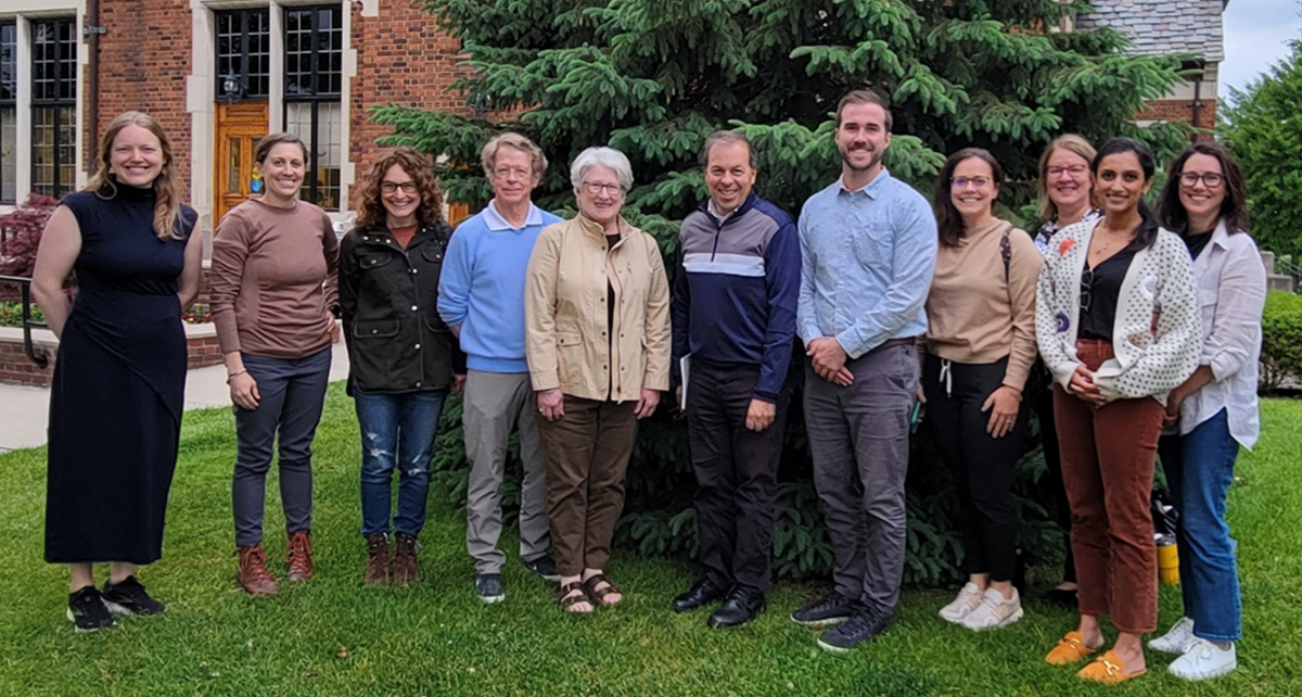 Ad hoc sustainability committee standing in group in front of brick building and pine tree.