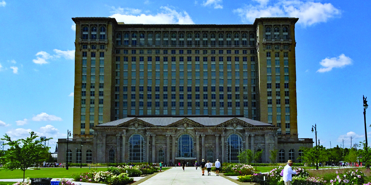 michigan central station People milling about, looking at flowers in front Towering historic brick building.
