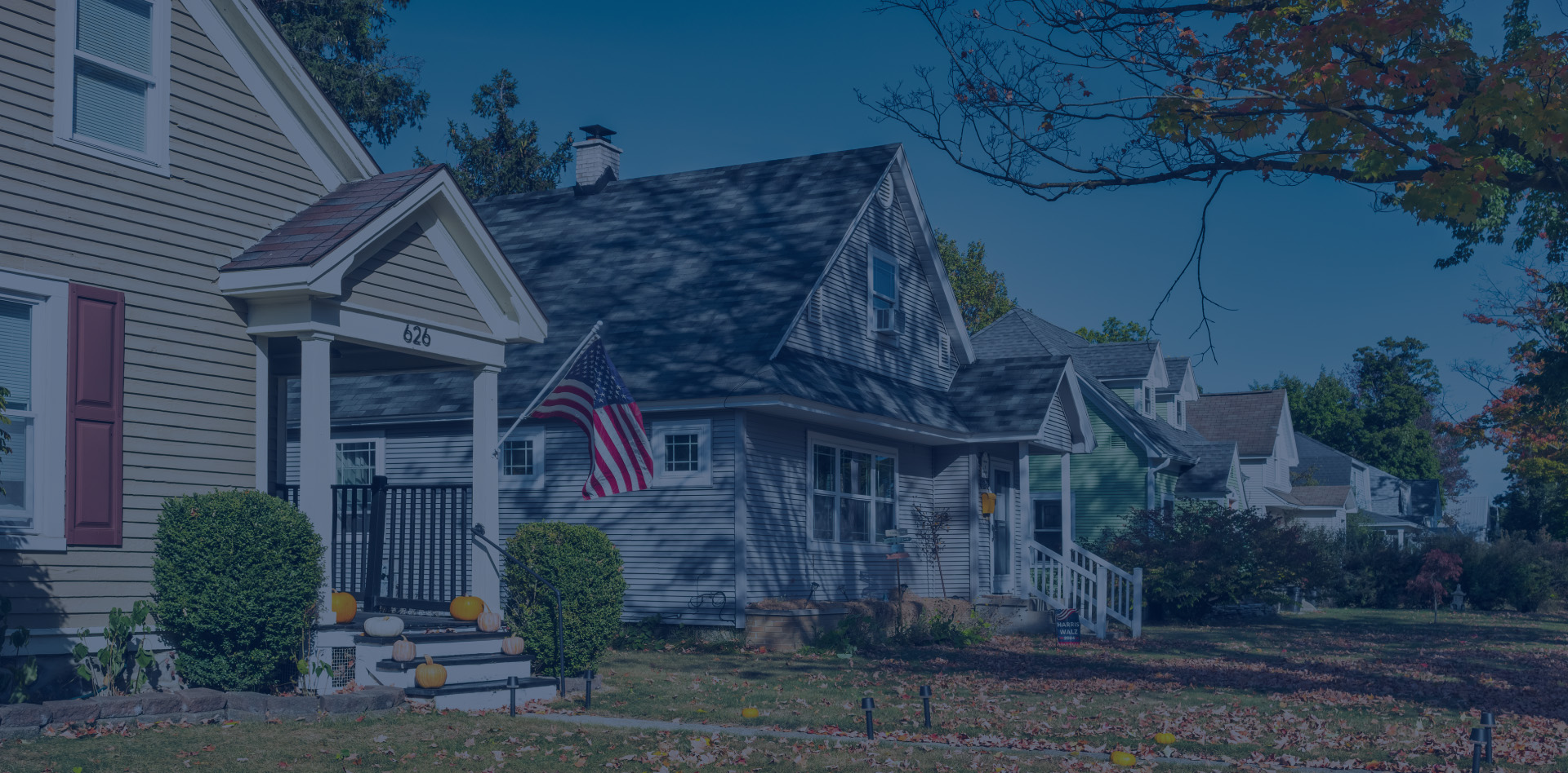 A street with houses and one has an american flag flying on the porch.