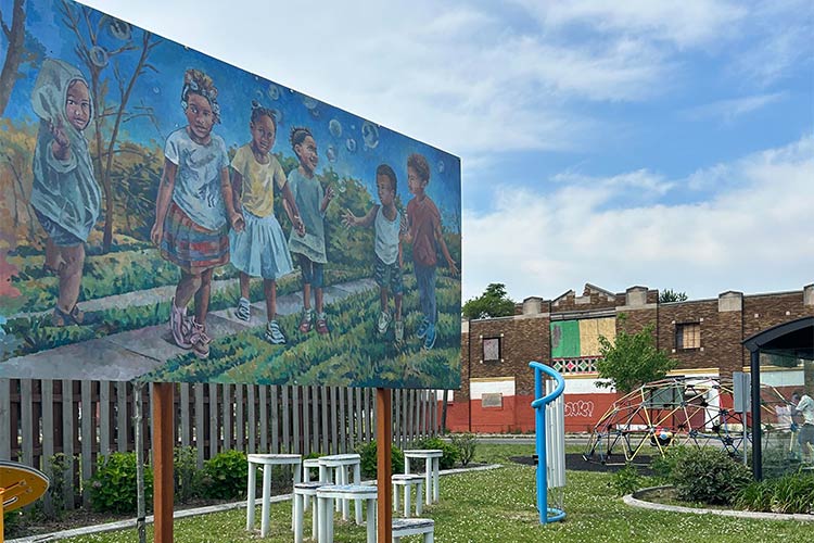 A garden with playground equipment, plants, and a large mural of children playing.
